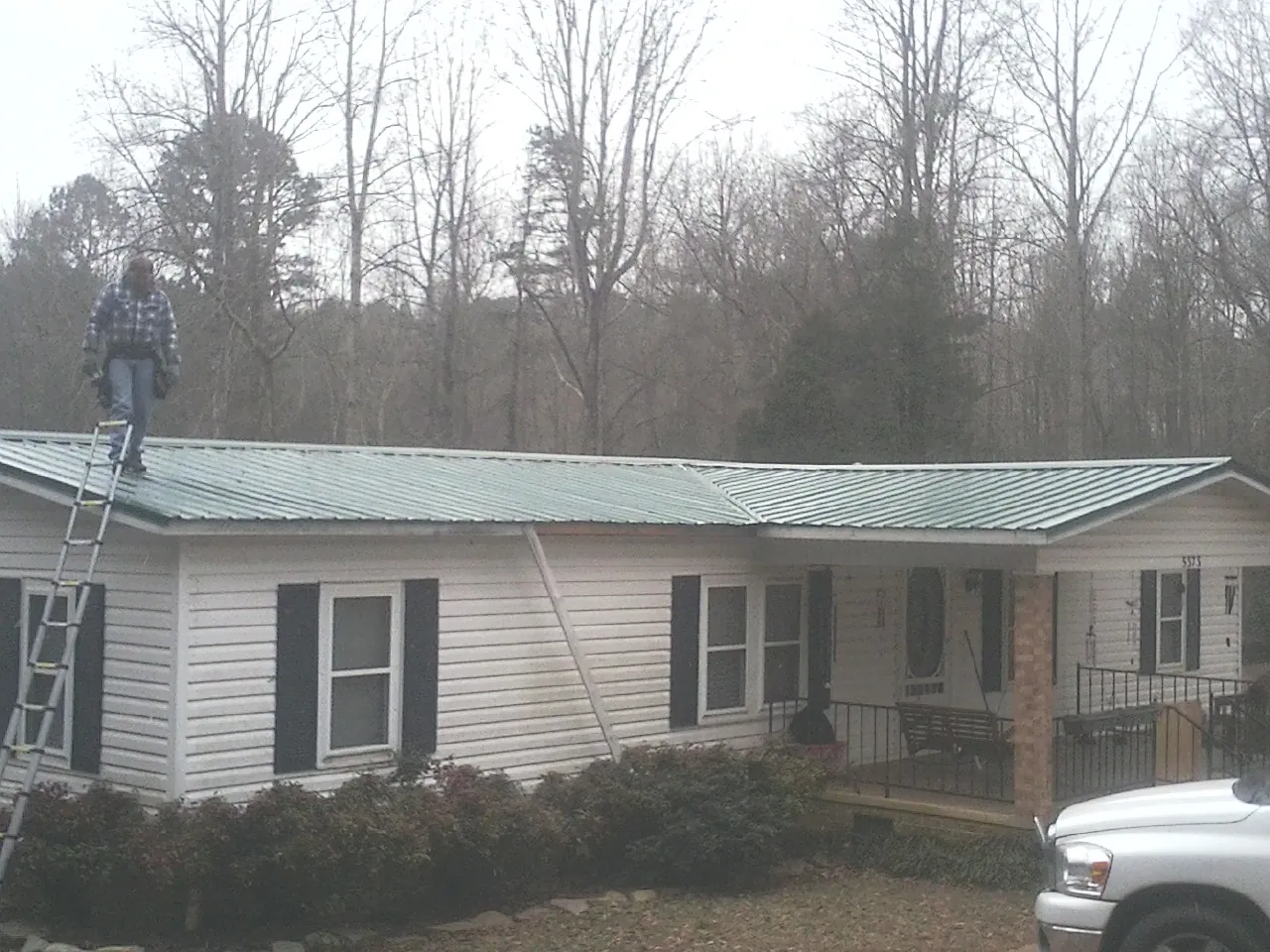 Worker on a ladder beside a new green metal roof on a ranch home in Eden